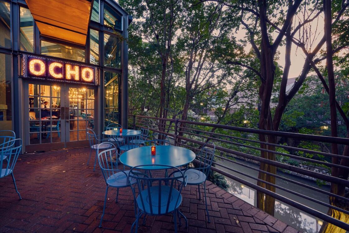 A view of the outdoor patio at Ocho with blue table and chairs in the foreground