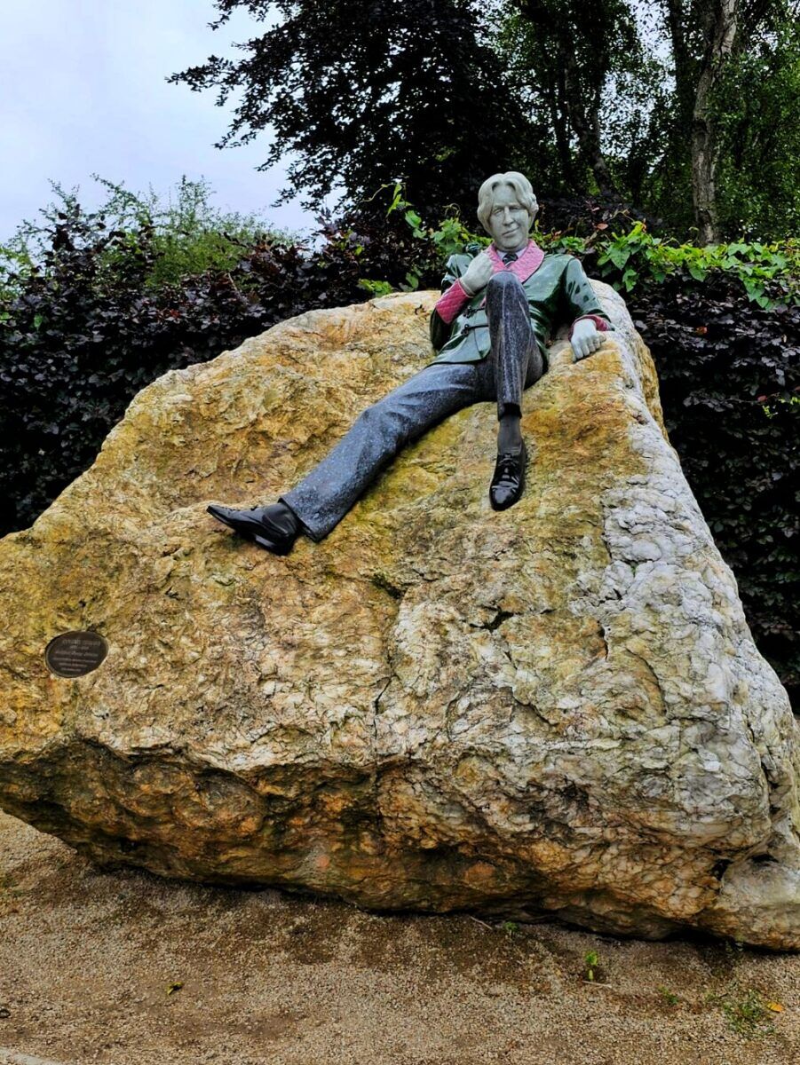 Life-size statue of Oscar Wilde reclining on a giant boulder