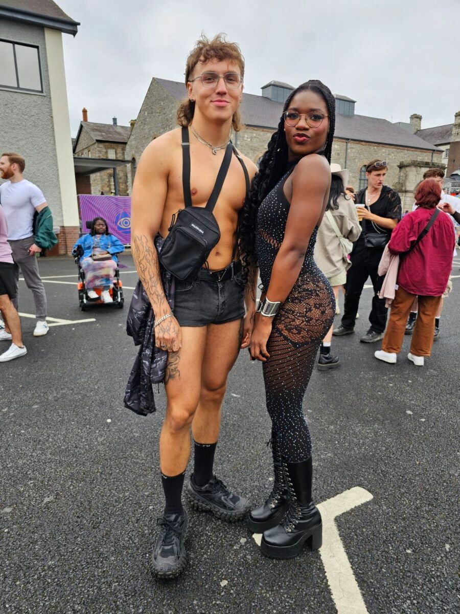 Two people, one in black leather, the other in lacey see-through pants stand on the street