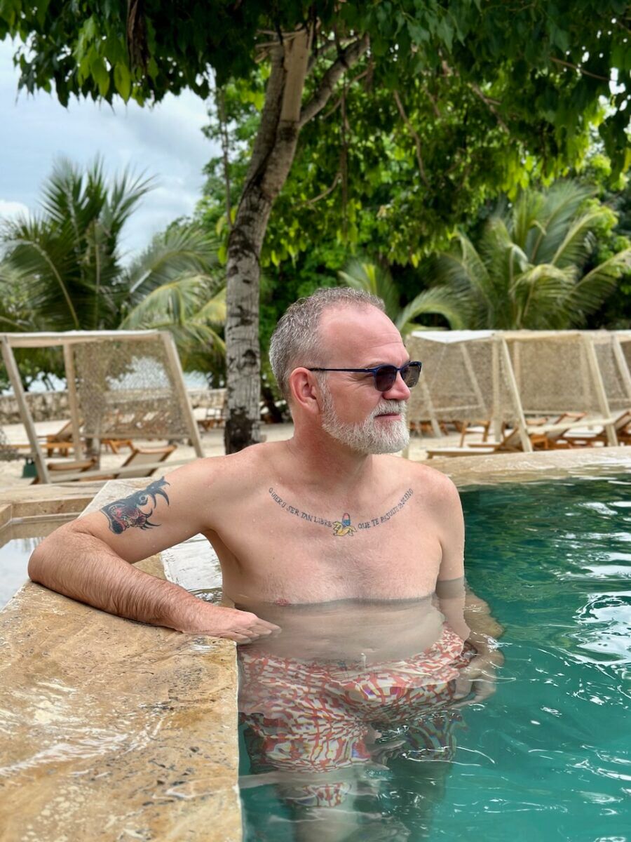 Bil Browning relaxes in a pool with one arm on the side of the pool and a beach in the background.