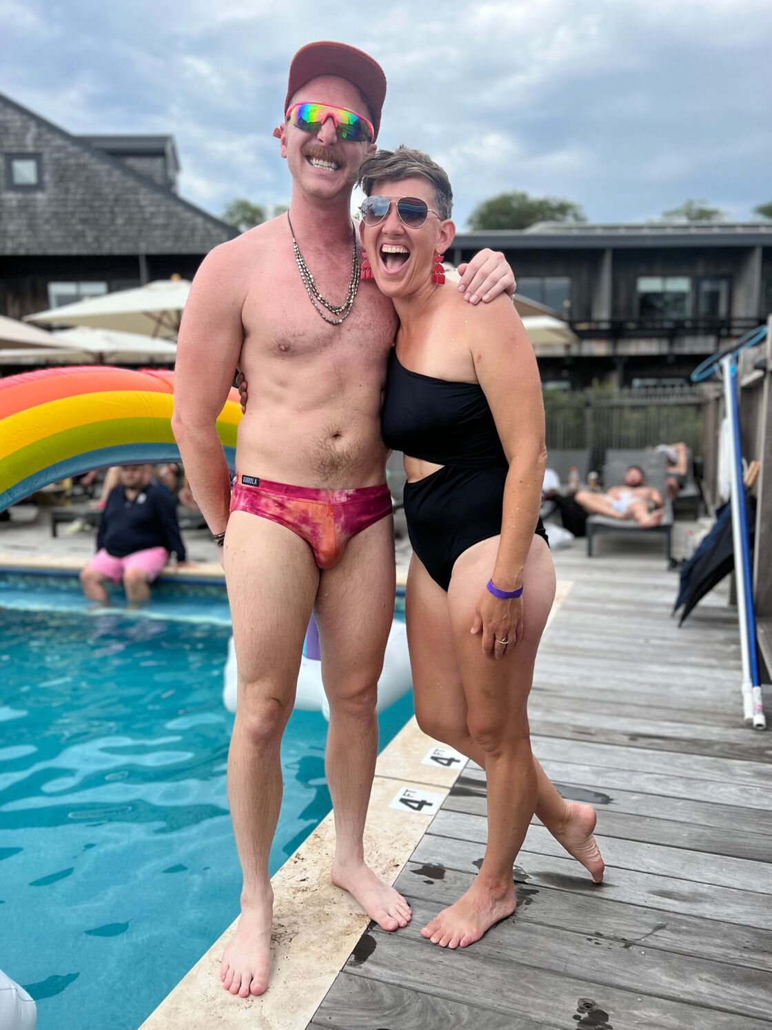 Two young people in swimsuits pose next to the pool