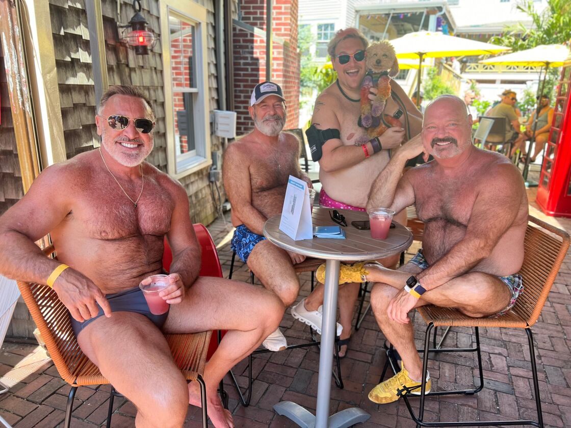 Four shirtless men gather around a small table and smile for the camera