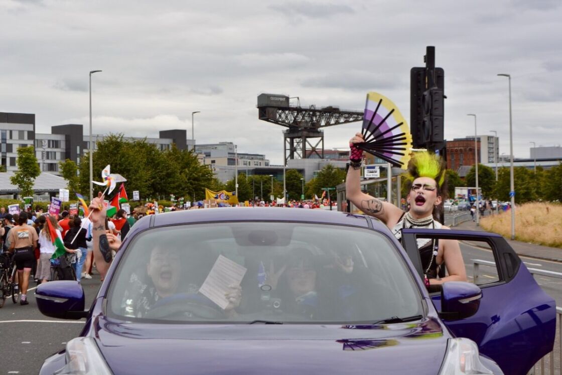 A punk with a yellow mohawk leanes out of a car and yells with pride