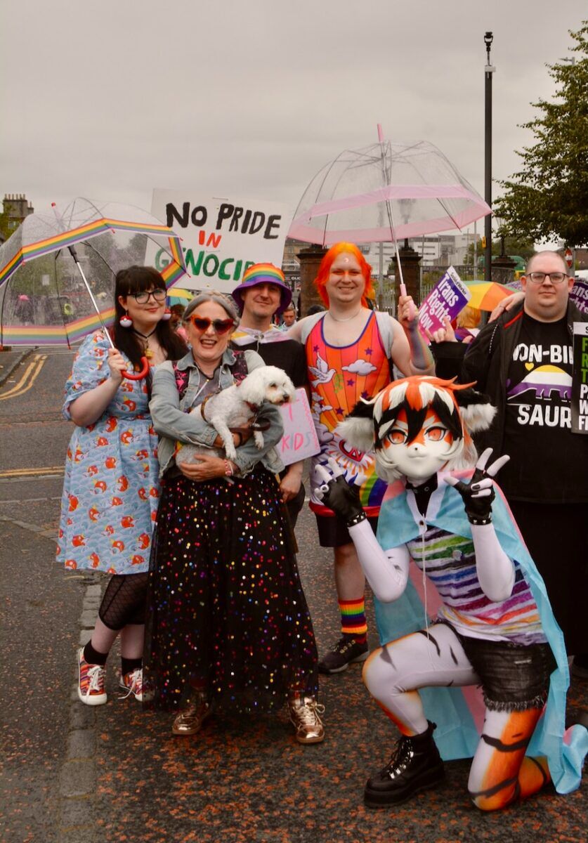 A group of people, including a furry, stand in the rain