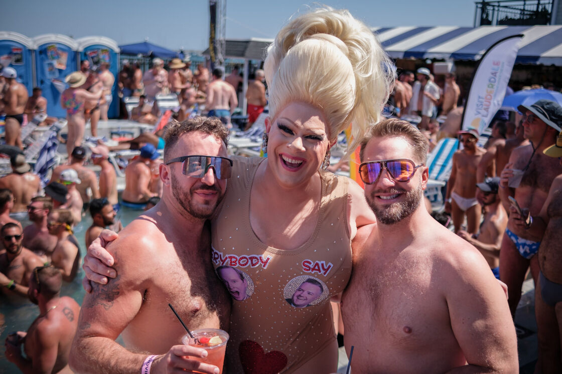 Drag queen posing with two men at a pool party.