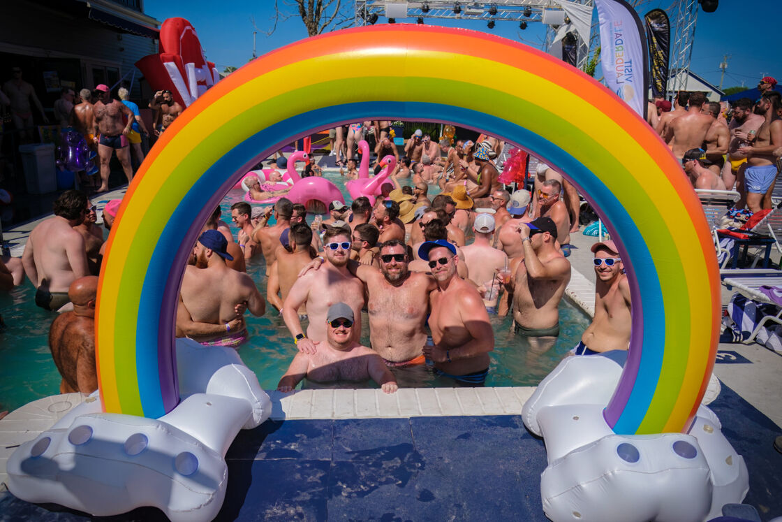 Group of men posing with a rainbow pool float in the pool.