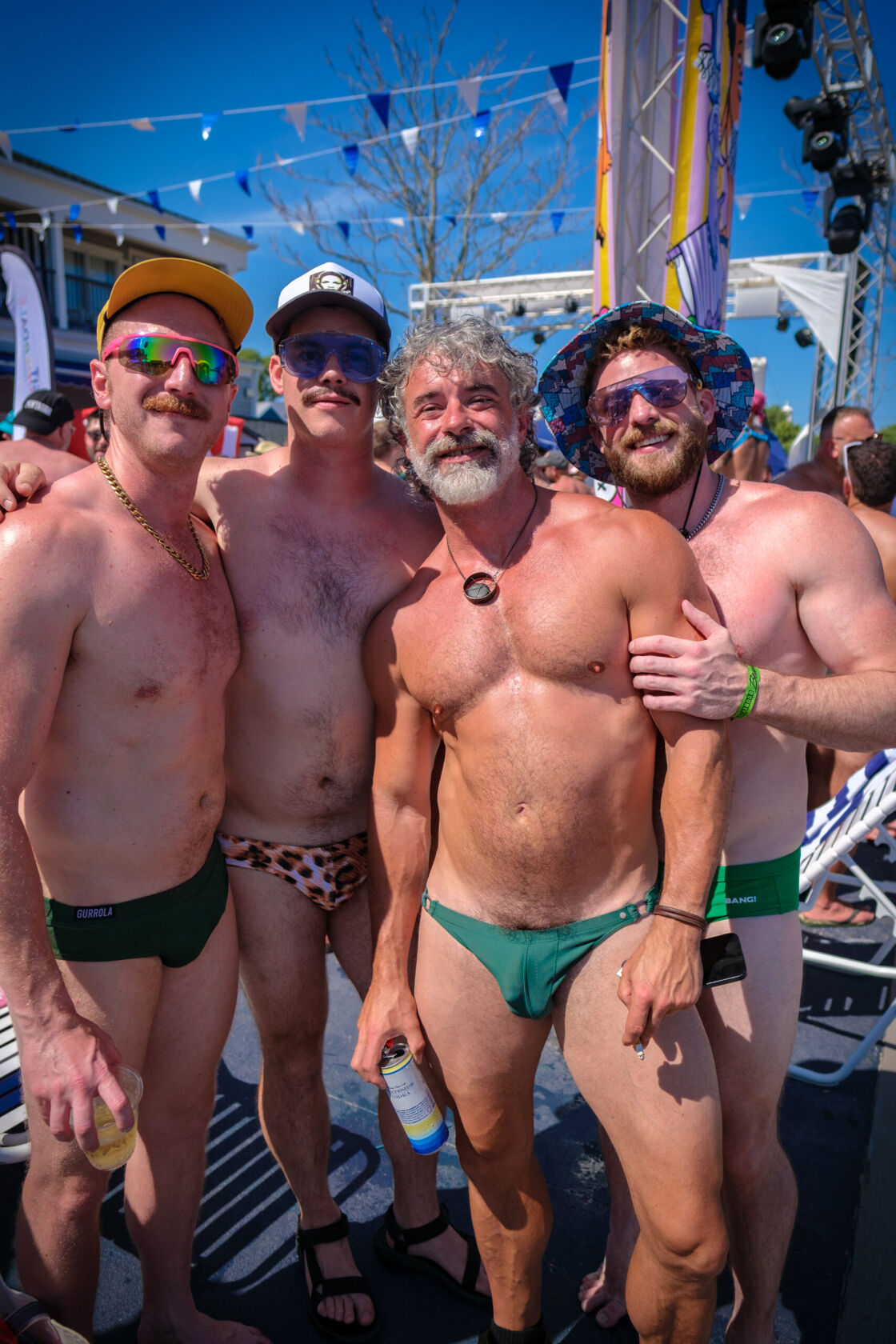 Group of men in Speedos posing together at a pool party.