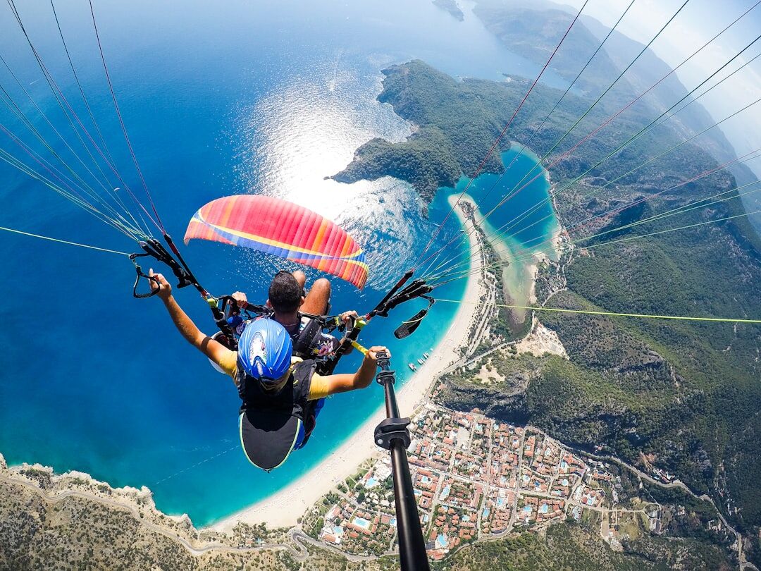 man in blue and black jacket riding on blue and white parachute An aerial view of the Blue Lagoon underneath a person paragliding