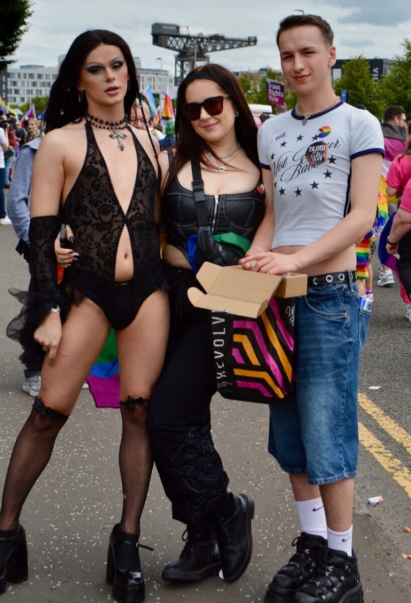 Three young people pose in the street during the Glasgow Pride parade.