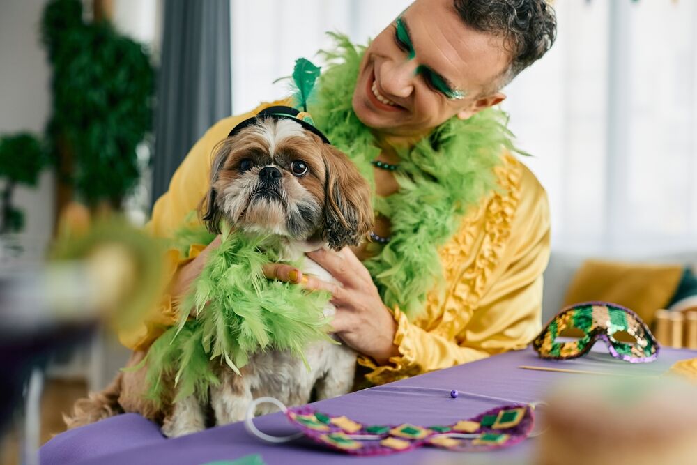 A young man wearing a yellow shirt and green eyeshadow sits at a table with a small dog