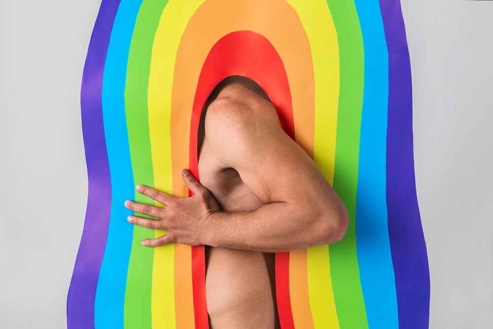 A naked muscular man stuck in an arch with rainbow pattern