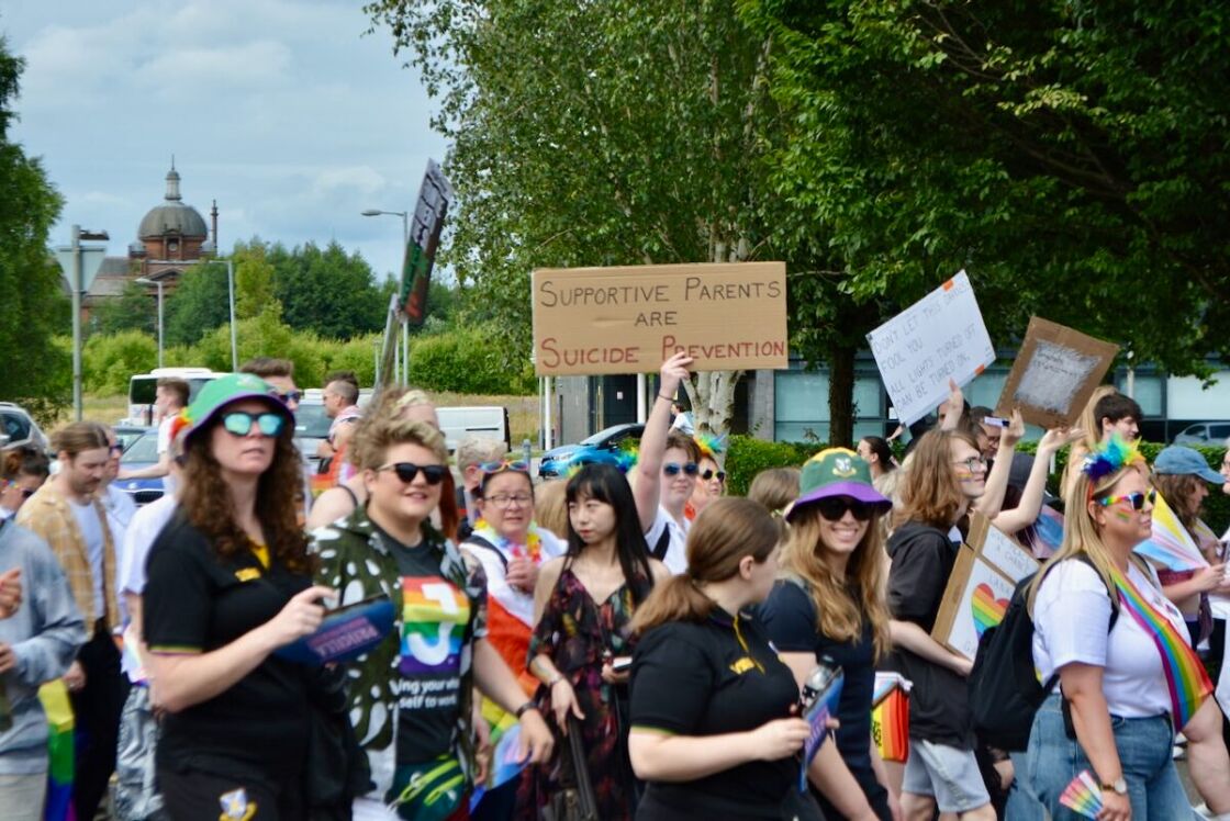 A crowd of people in Glasgow march in the the Pride parade. One holds a sign that reads "Supportive parents are suicide prevention."