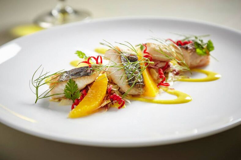 A refined and expertly plated dish. There are small pieces of blackened fish, dill leaves and mandarin slices. The colors are bright and vibrant