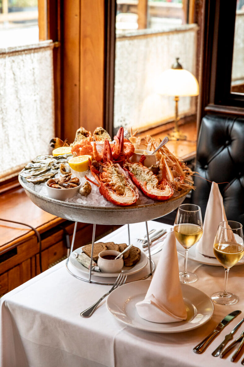 A stunning seafood tower next to two glasses of white wine placed on a white linen tablecloth . 