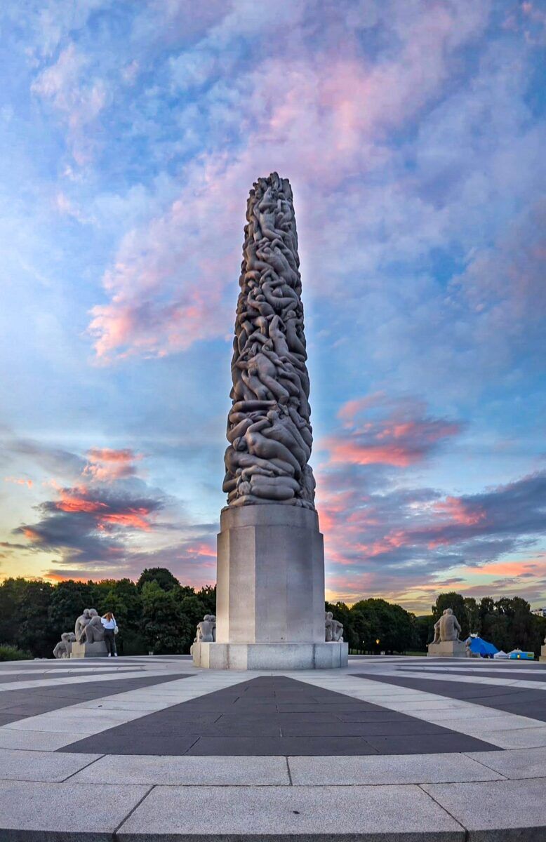 The Monolith with a colorful sunset behind it. A statue at Vigeland Sculpture Park