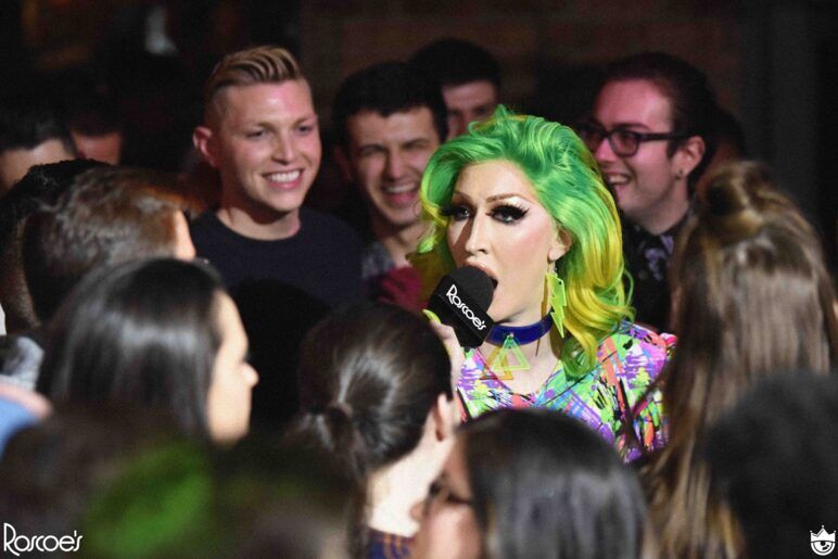 A hilarious drag queen with bright green hair entertains a happy crowd.