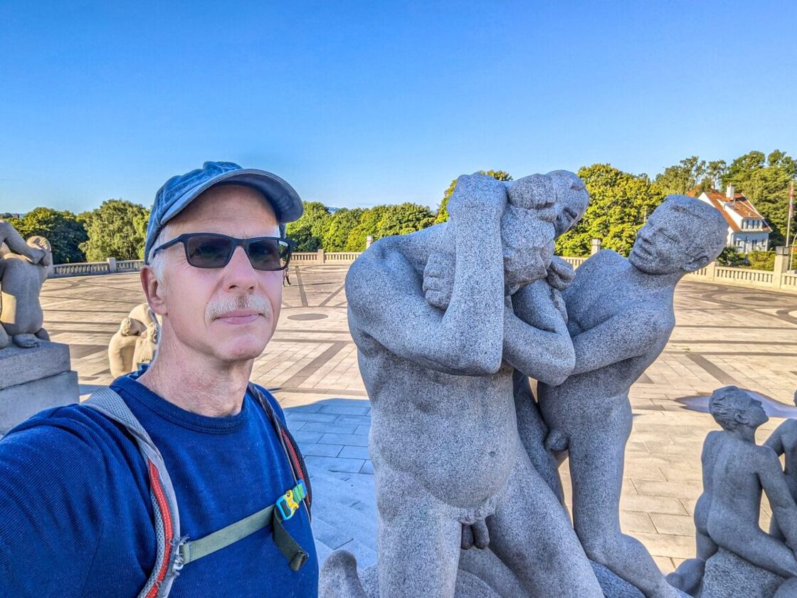 Michael standing next to a granitce sculpture depicting two boys assaulting a man. The author stands in front of a statue at Vigeland Sculpture Park