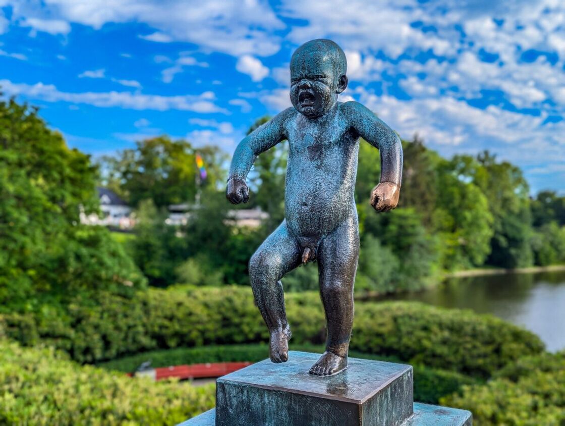 Bronze sculpture of Angry Baby with the park in the background. A statue at Vigeland Sculpture Park