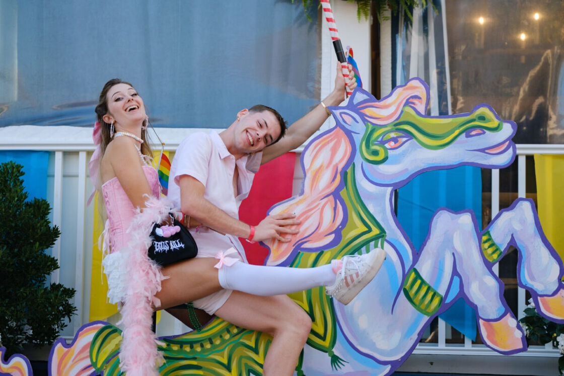 Two friends smile while posing on a large wooden unicorn