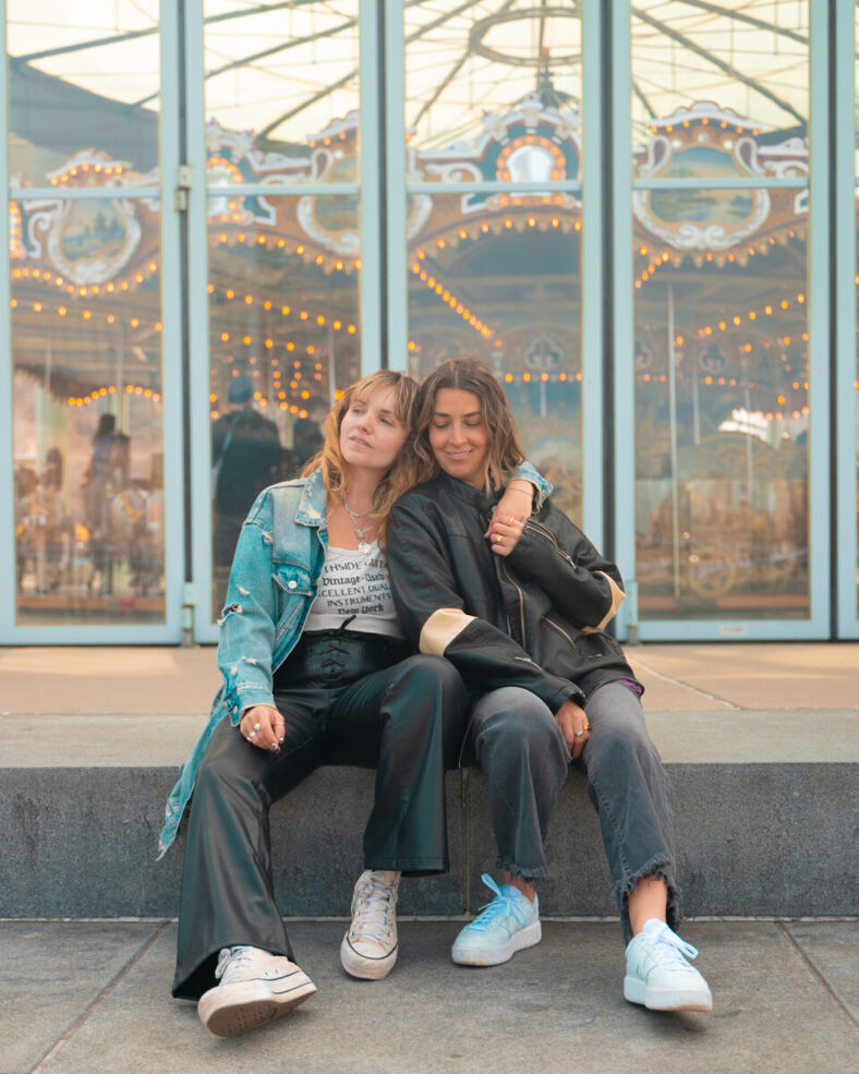 Gabi and Shanna sit together in front of windows with a carousel reflected in the glass