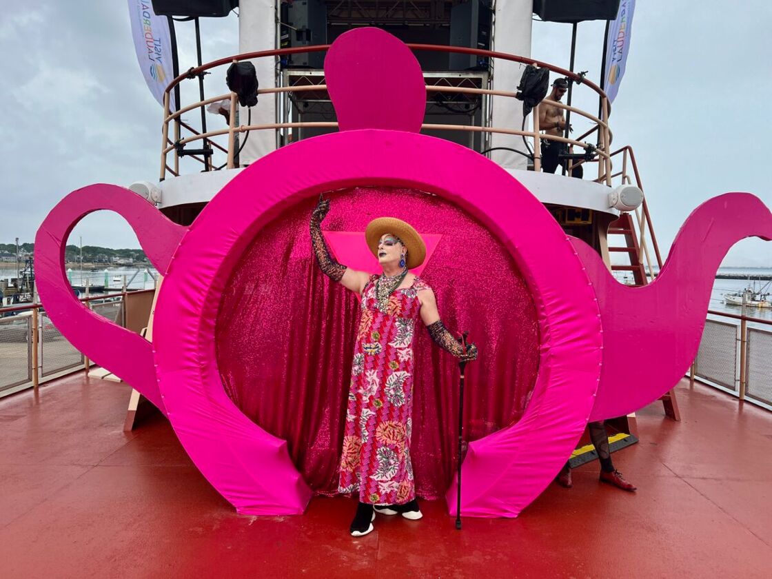 A fabulous queen in bright pink stands in front of a large teapot doorway