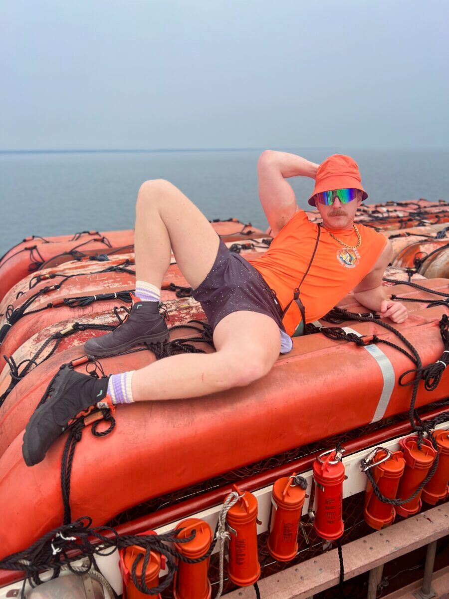 A man in bright orange poses on top of boat safety equipment