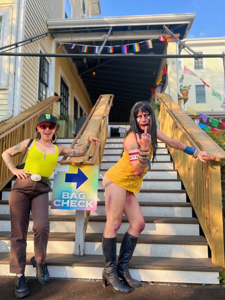 Two people with lots of energy stand on the steps next to a bag check sign.