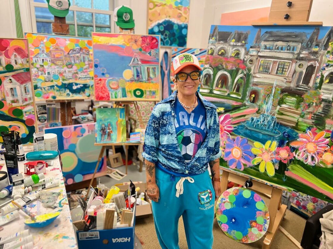 An artist stands in front of their colorful artwork