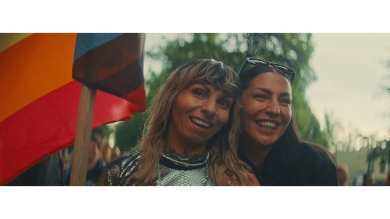 Two women embrace under a Pride flag