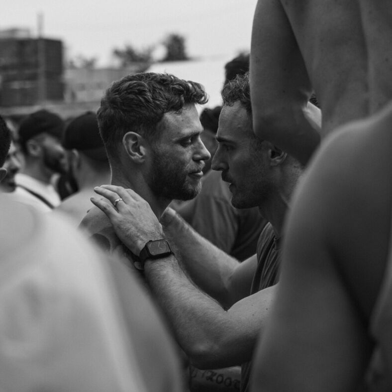 Black and white photo of two men dancing together as seen through a crowd