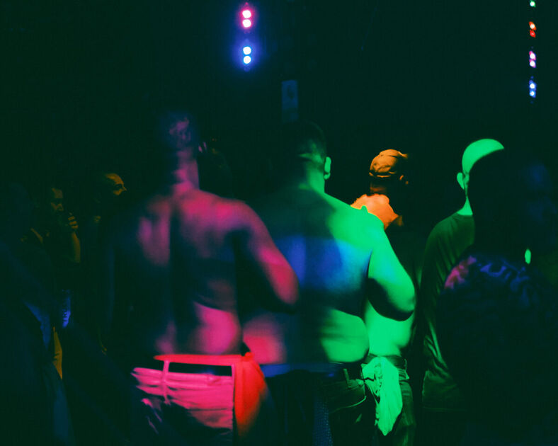 Two men's backs are lighted by green and red lights.