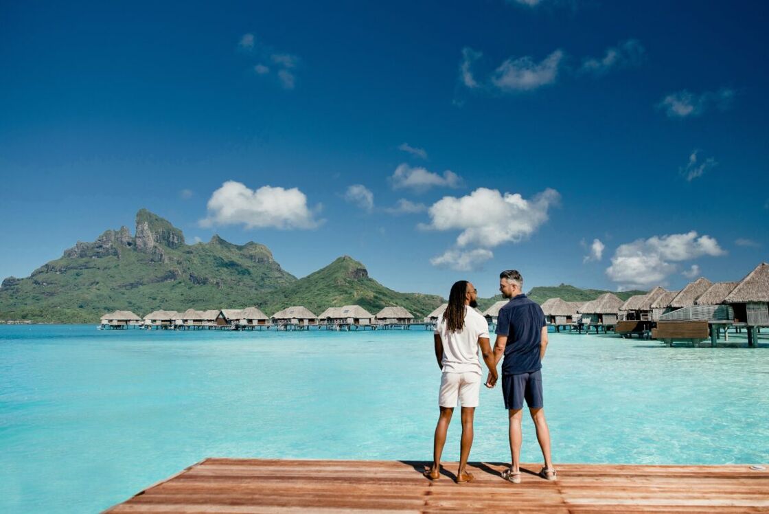 A male couple holds hands on a dock in Bora Bora, French Polynesia.