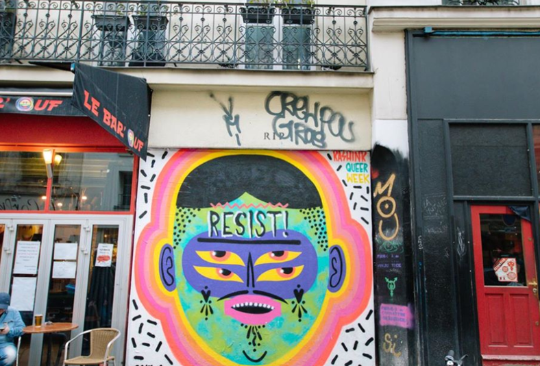 The exterior of La Mutinerie painted with a vibrant image and the word 'resist!' written on the wall.