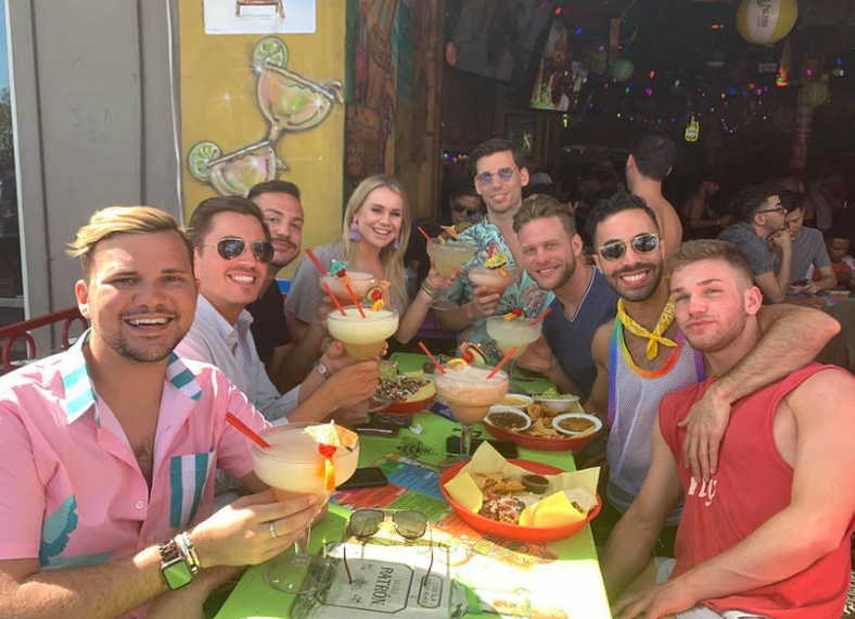 A group of friends sit on a packed patio with margaritas in hand and food on the table. Photo via Fiesta Cantina