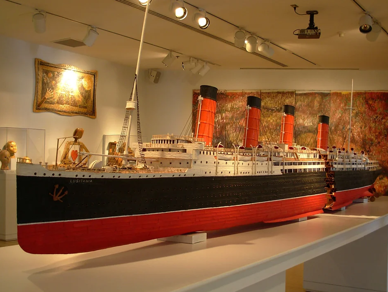 A massive steamer ship replicated entirely from toothpicks sits on a large table illuminated by light. 