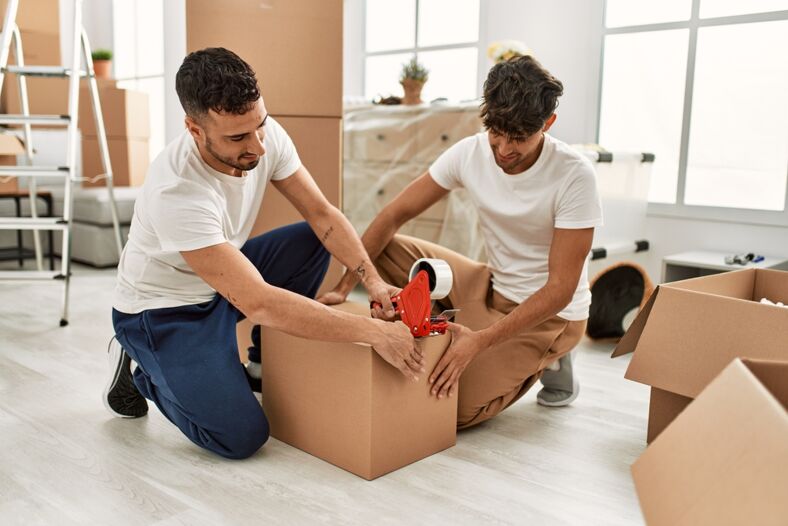 Two Hispanic men packing a box in preparation for a move