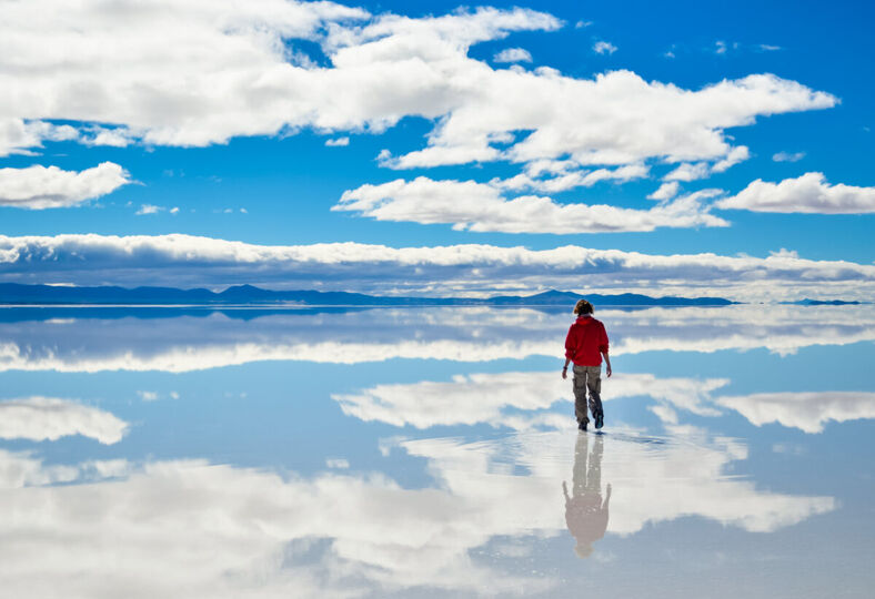 Girl walking on the mirror surface of Salar de Uyuni in Bolivia with clouds reflections