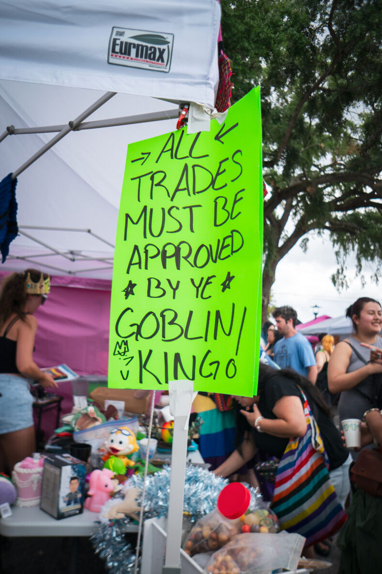 A neon green sign attached to a tent pole reads 'All trades must be approved by ye Goblin King!'
Photographer: Tyler Koran