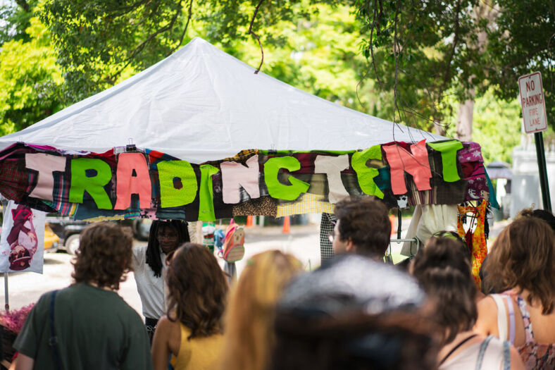 A large patchwork sign reading 'Trading Tent' with a large crowd in front of it. Photographer: Tyler Karon