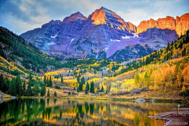 A stunning view of a lake surrounded by changing leaves and a massive mountain range being lit by the sun