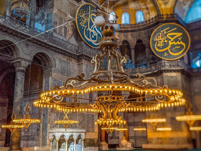 The soft golden lights of a chandelier inside Hagia Sophia. A giant chandelier inside the Fatih mosque