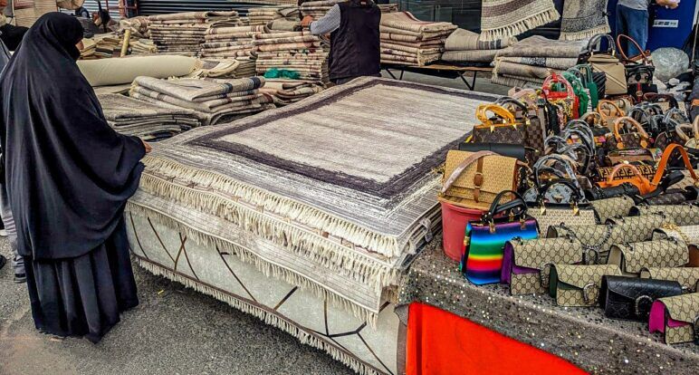 A woman in a burqa inspects a rug in an outdoor market