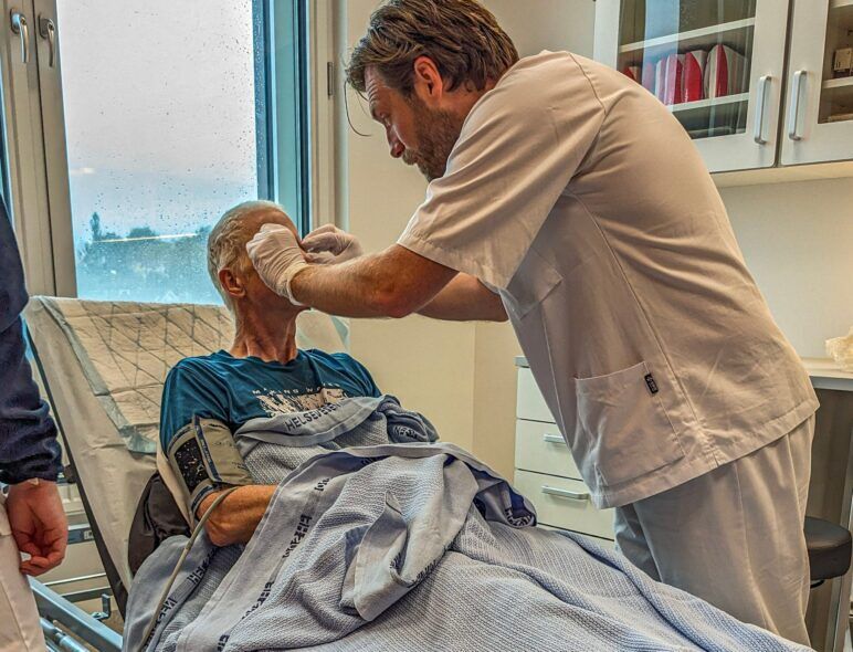 Michael in a hospital bed covered with blankets as the doctor removes my glasses. 