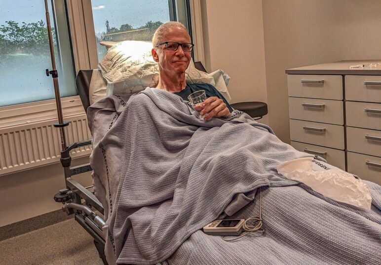 A smiling Michael sitting up in bed holding a glass of water. A smiling Michael sitting up in bed holding a glass of water.