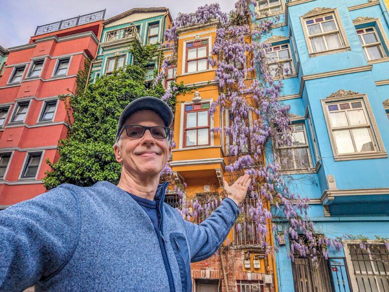 Michael standing in front of buildings painted green, blue, yellow, and orange. Street view of colorful houses in Balat