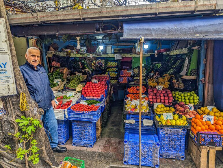 A fruit and vegetable vendor stands in the doorway of his stall