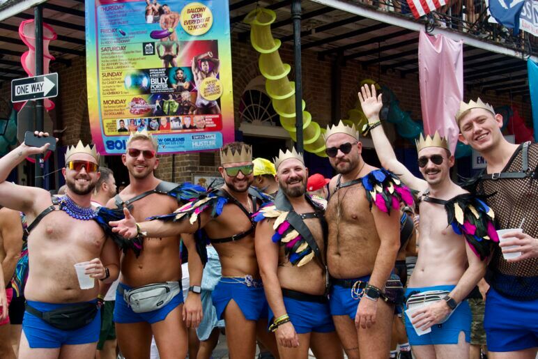 A group of men in feathered harnesses all wear gold crowns and smile for the camera