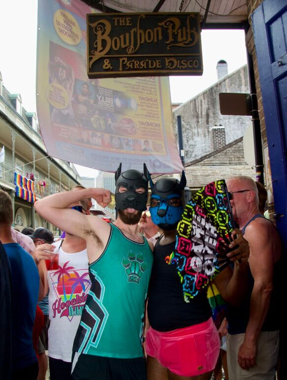 Two lovers of puppy play wear the signature masks and pose underneath the sign for The Bourbon Pub.