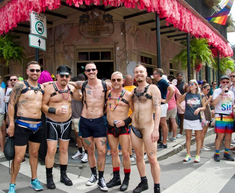 Four scantily clad men, all sporting harnesses stand in the busy street