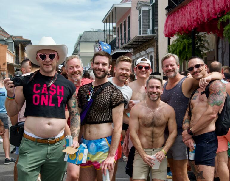 A group of friends all smile broadly for the camera in the middle of the packed street